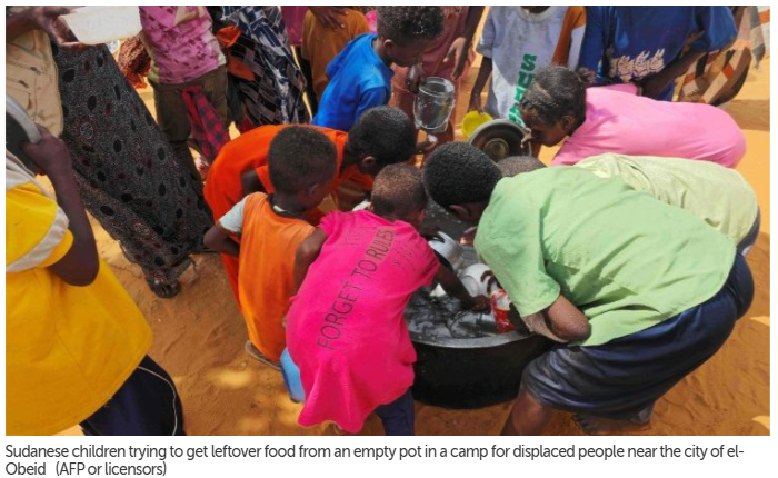 Sudanese children trying to get leftover food from an empty pot in a camp for displaced people near the city of el-Obeid  