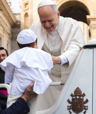 Pope Leo reaching out to a baby dressed like him in white