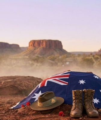 Australian flag draped over a burial mound with a army slouch hat and army boots to the side